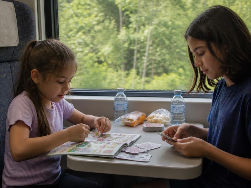 Kids playing cards and sticker books at a train seat table during a long ride