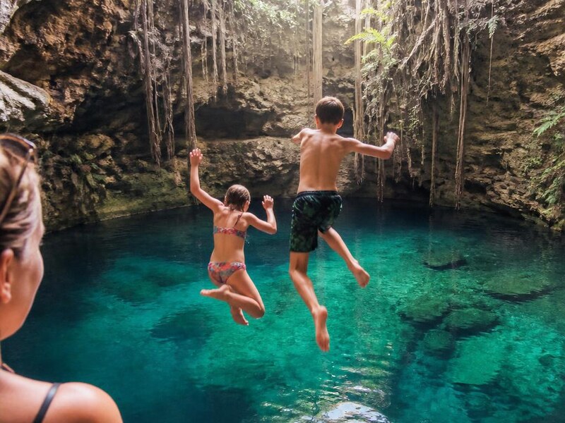 Two children jumping into the clear turquoise water of a cenote near Tulum